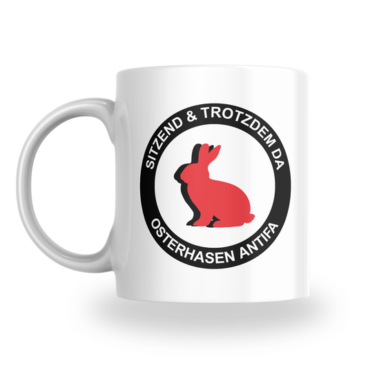 „Sitzend & trotzdem da – Osterhasen Antifa“ – Keramiktasse (325 ml)